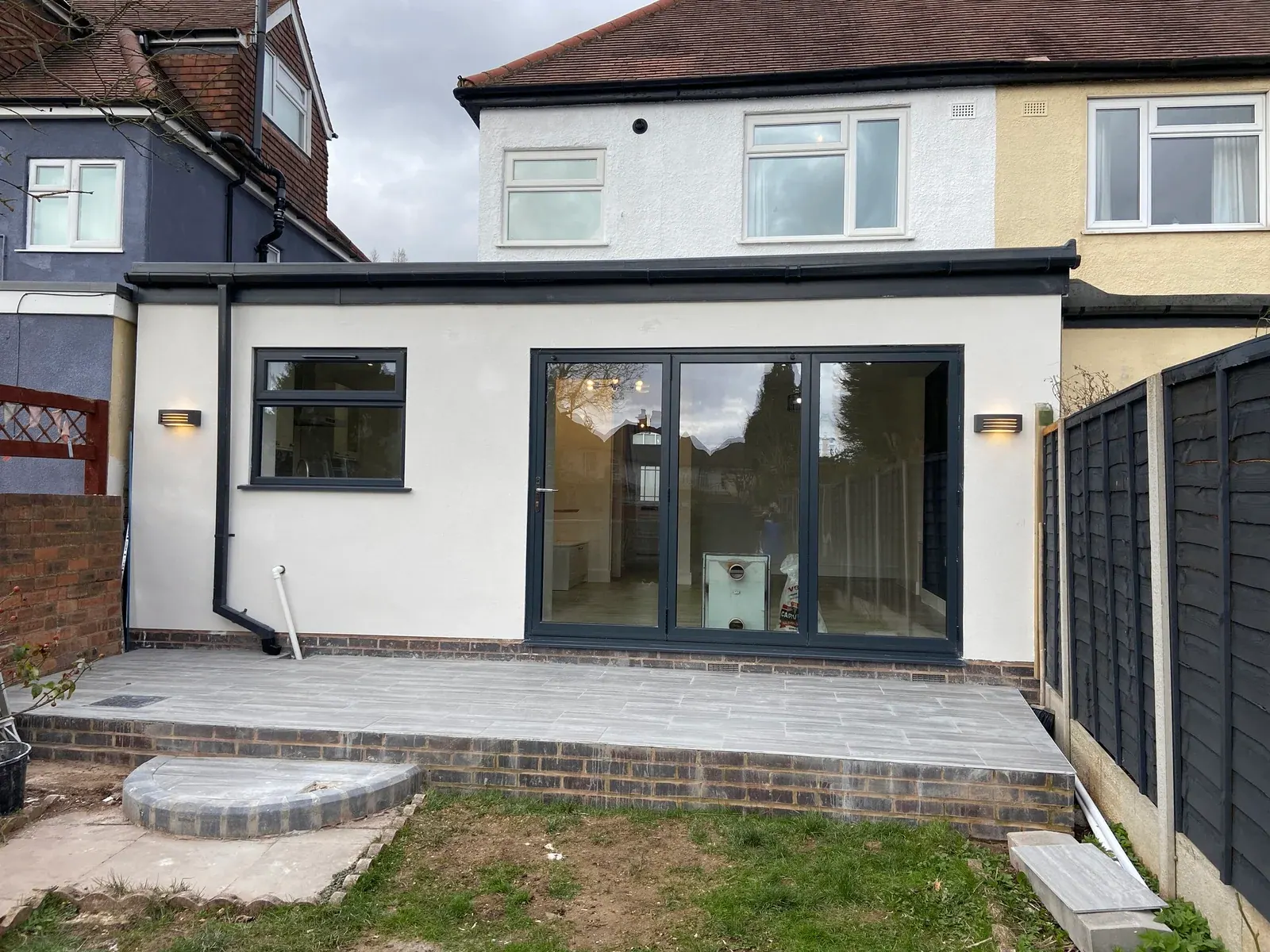Single-storey rear extension with rendered walls, grey bi-fold doors and a raised tiled patio