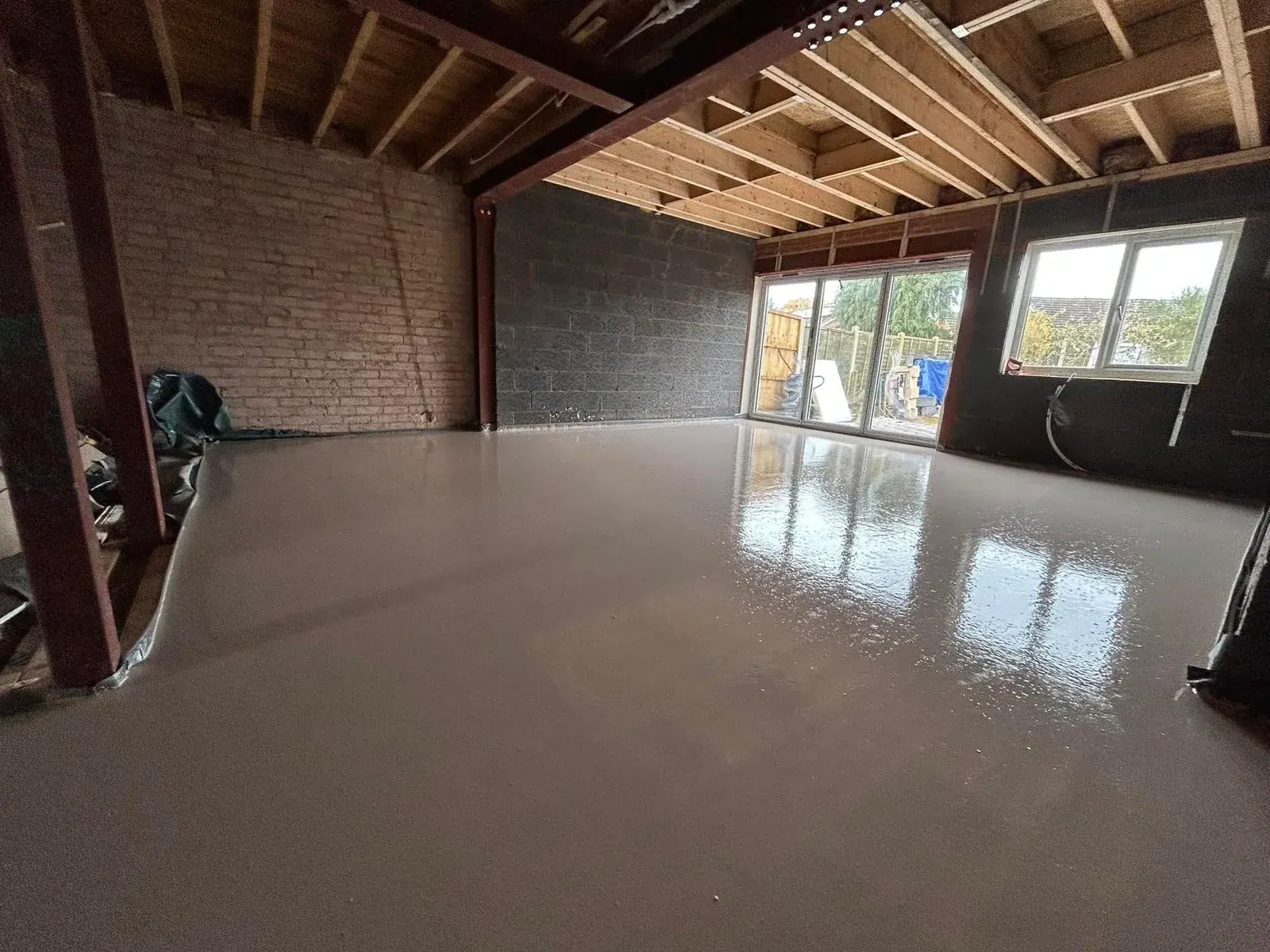 Freshly poured screed floor in an extension, with exposed roof joists, steel beams and sliding doors